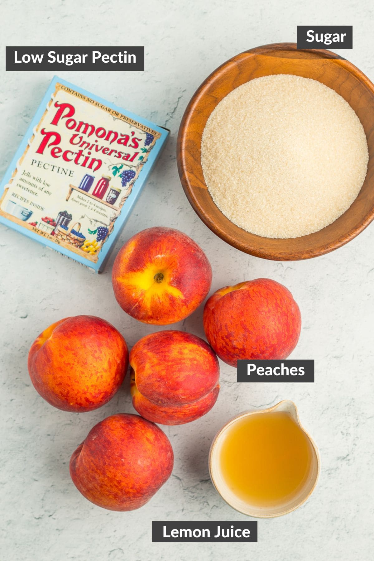 a bowl of sugar, a box of pectin, a small bowl of lemon juice, and 5 peaches on a board.