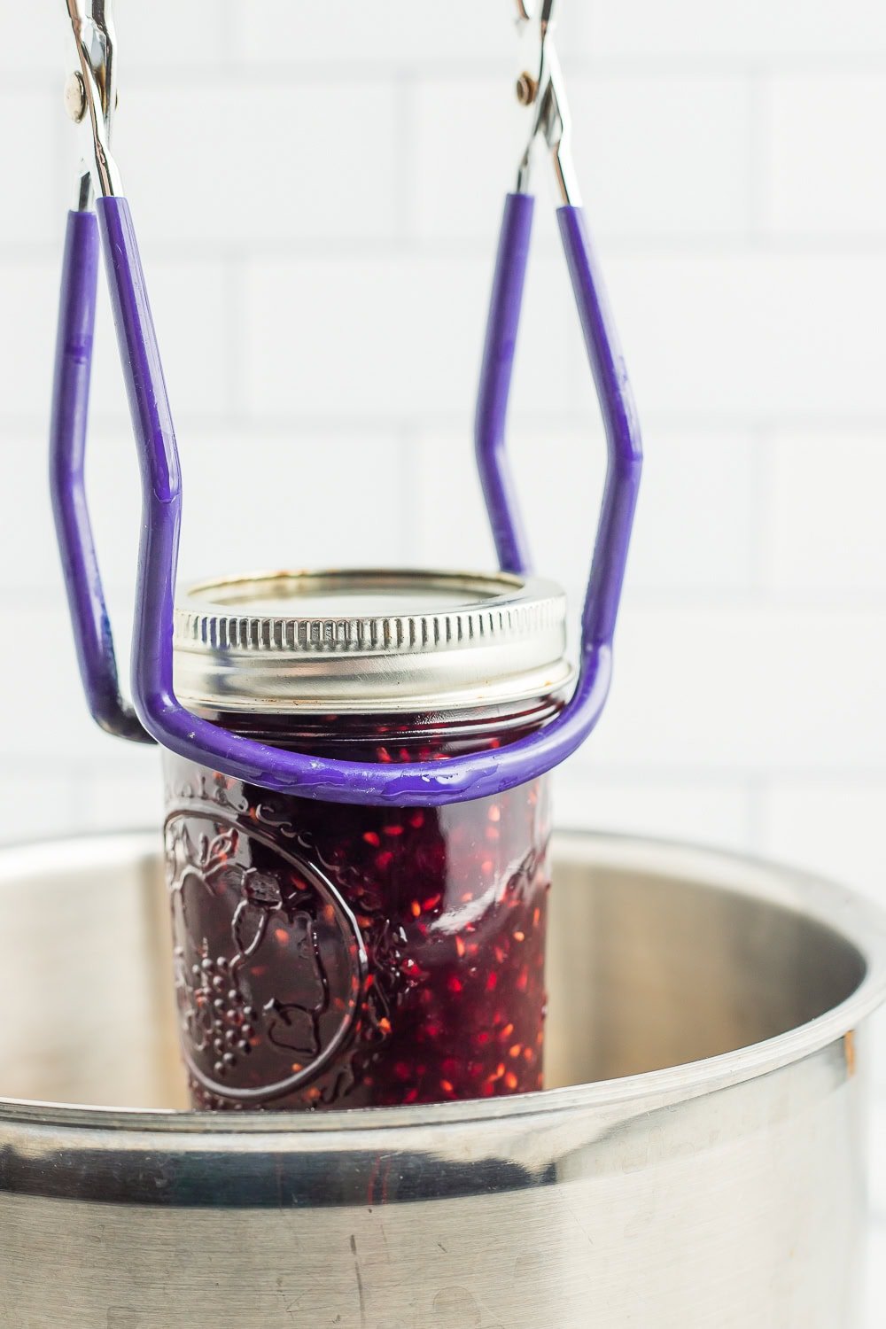 canning tongs holding a jar of preserves over a canner.