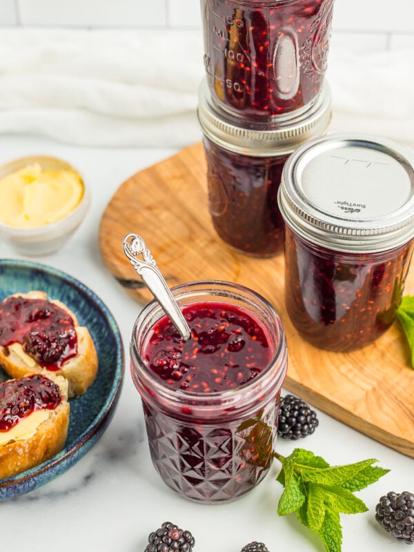 4 jars of blackberry jam with fresh blackberries and a sprig of mint.