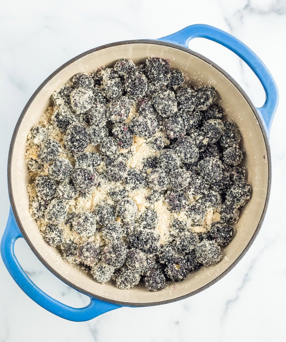 sugar mixed with berries in a blue Dutch oven.