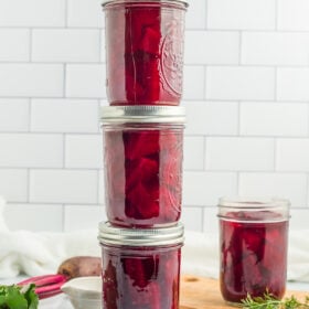 4 jars of canned pickled beets against a tile backsplash.