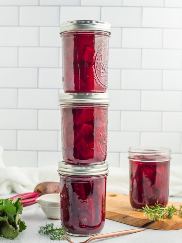 4 jars of canned pickled beets against a tile backsplash.