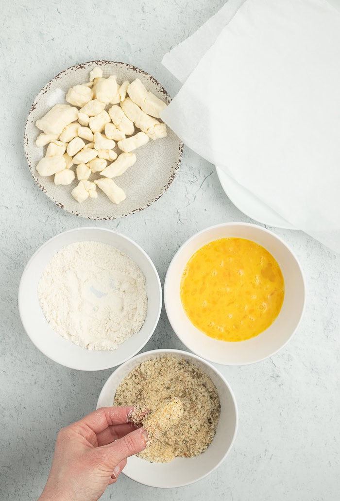 3 bowls of breading and a hand dipping something into a bowl of breadcrumbs.