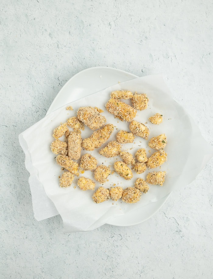 unbaked breaded cheese curds on a plate lined with parchment paper.