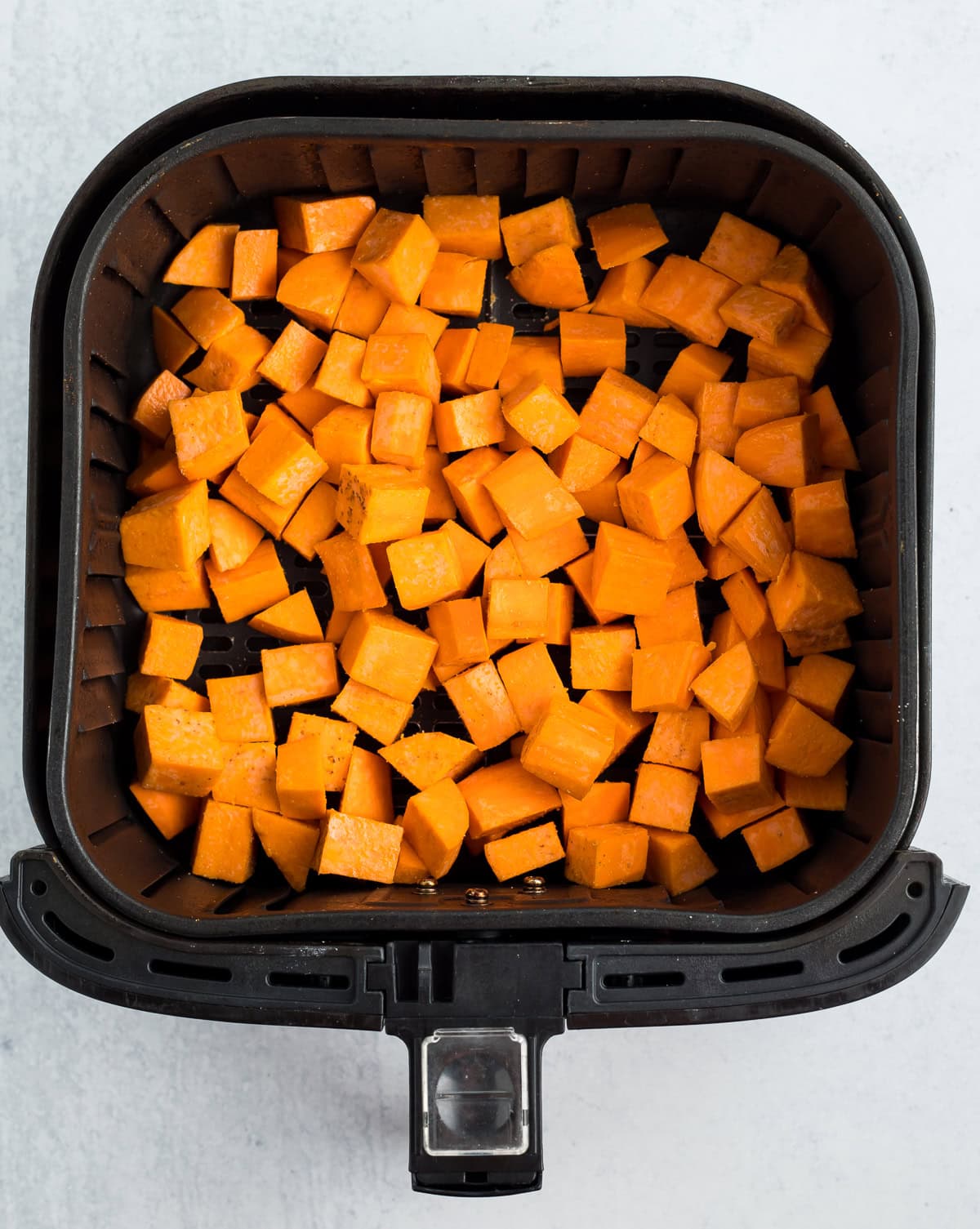 cubed uncooked sweet potatoes in an air fryer basket.