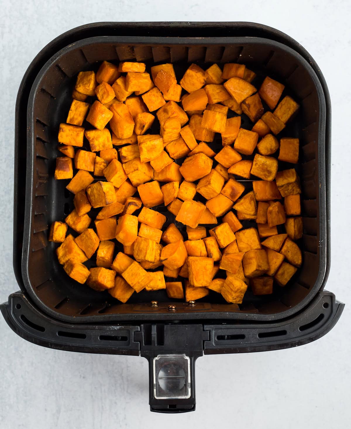 cubed baked sweet potatoes in an air fryer basket.