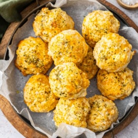 an overhead photo of a pan of cheddar bay biscuits on top of a wooden cutting board.