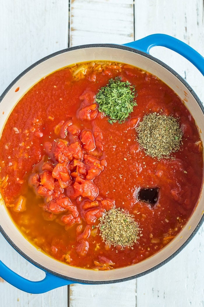 tomatoes, spices, and other ingredients in a blue Dutch oven.