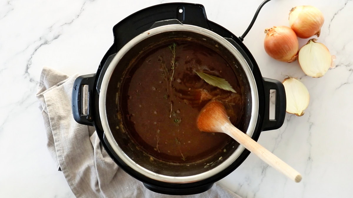 ingredients in a pressure cooker with a wooden spoon.