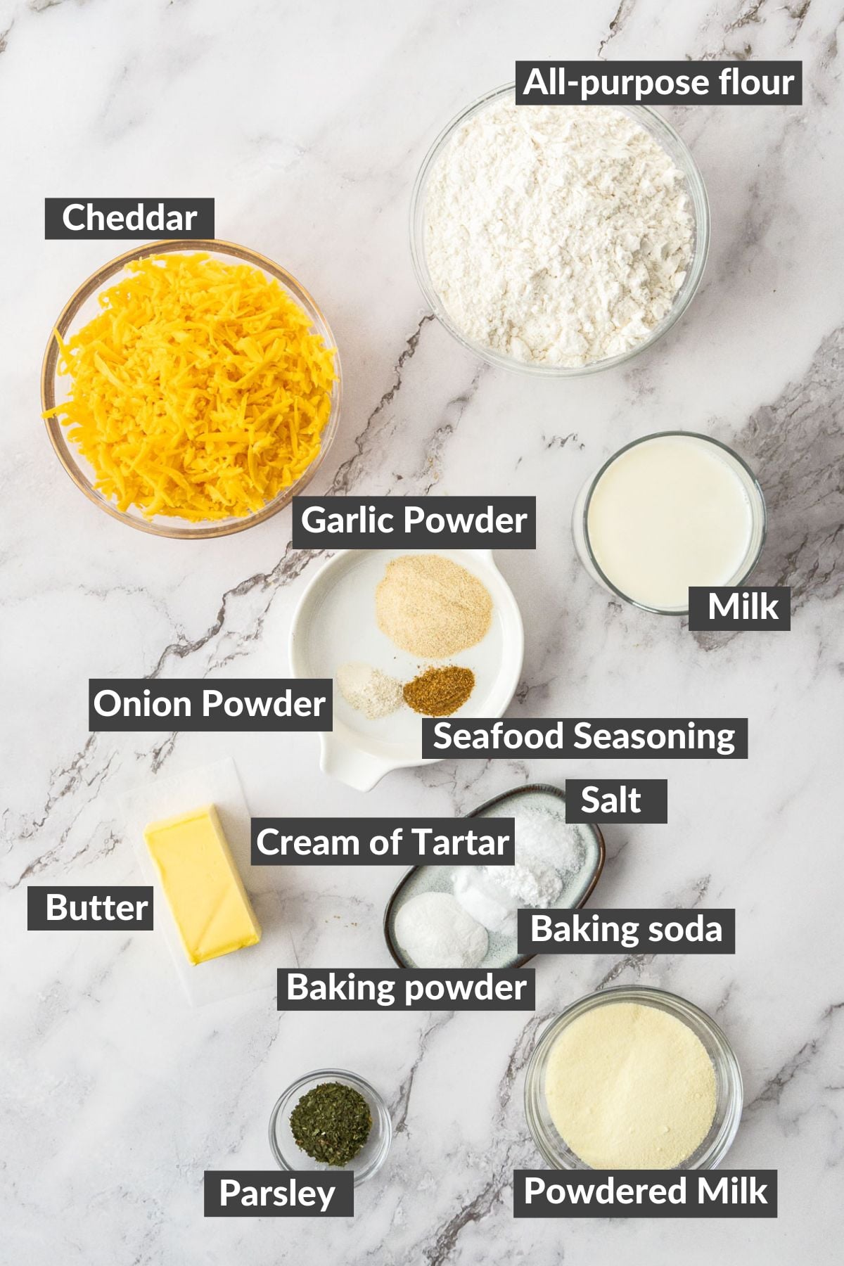 shredded cheese, flour, powdered milk, butter, and other ingredients on a marbled board.