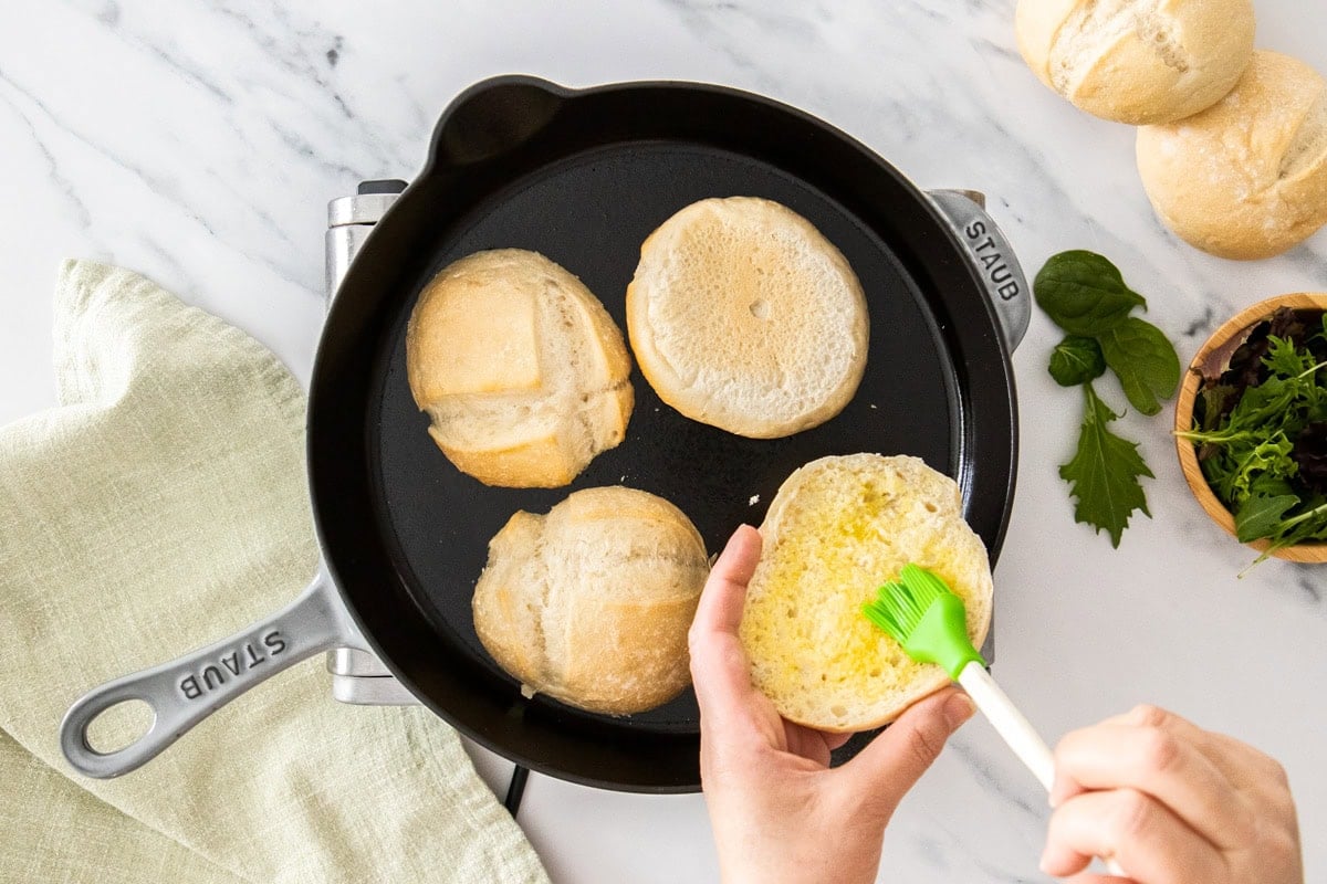 a pastry brush brushing olive oil on rolls in a skillet.