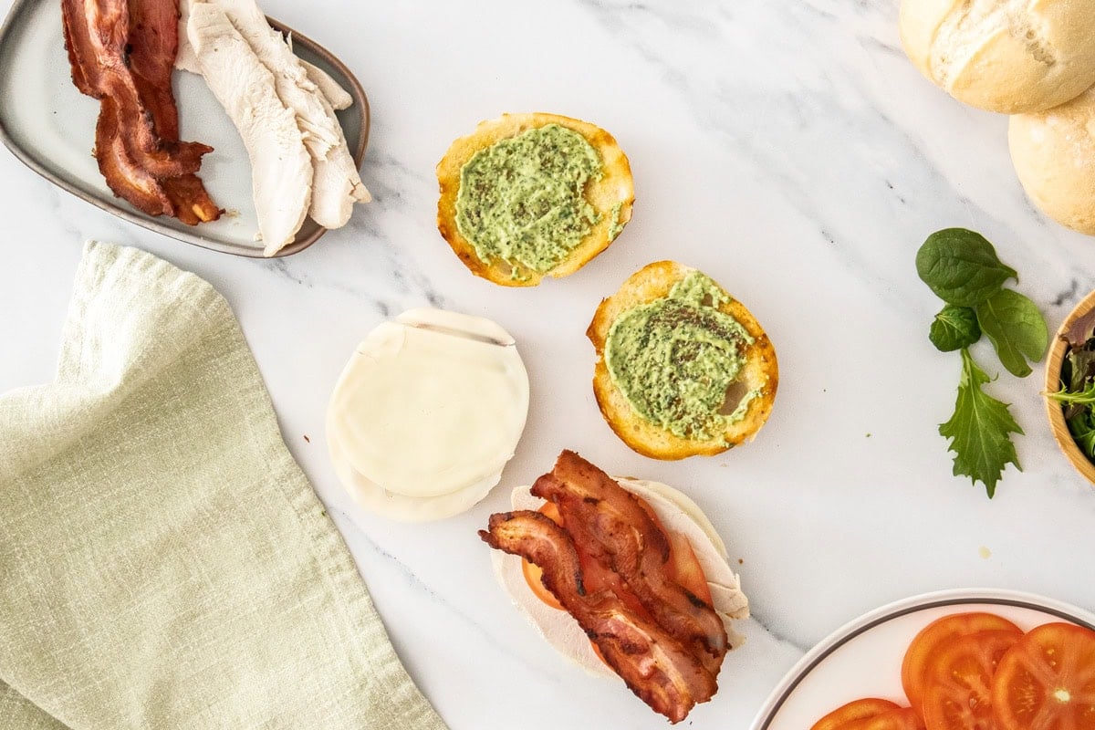 pesto mayo and other ingredients on rolls.