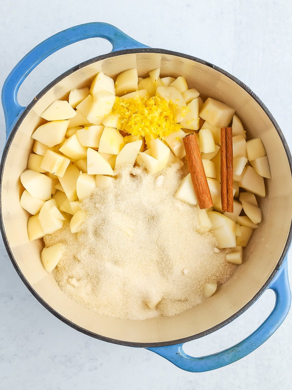chopped fruit, sugar, and cinnamon sticks in a blue Dutch oven.