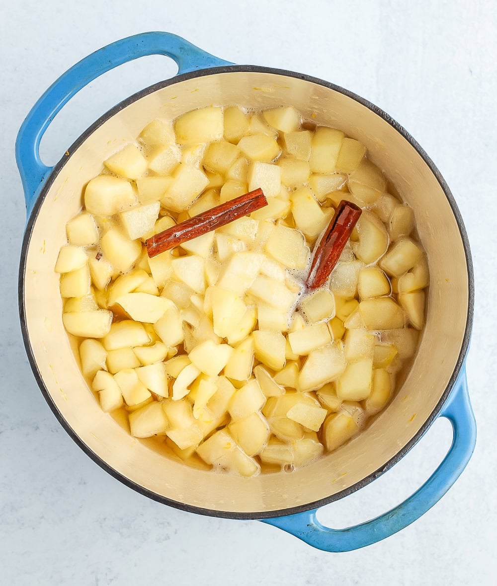 chopped fruit and cinnamon sticks simmering in a blue Dutch oven.