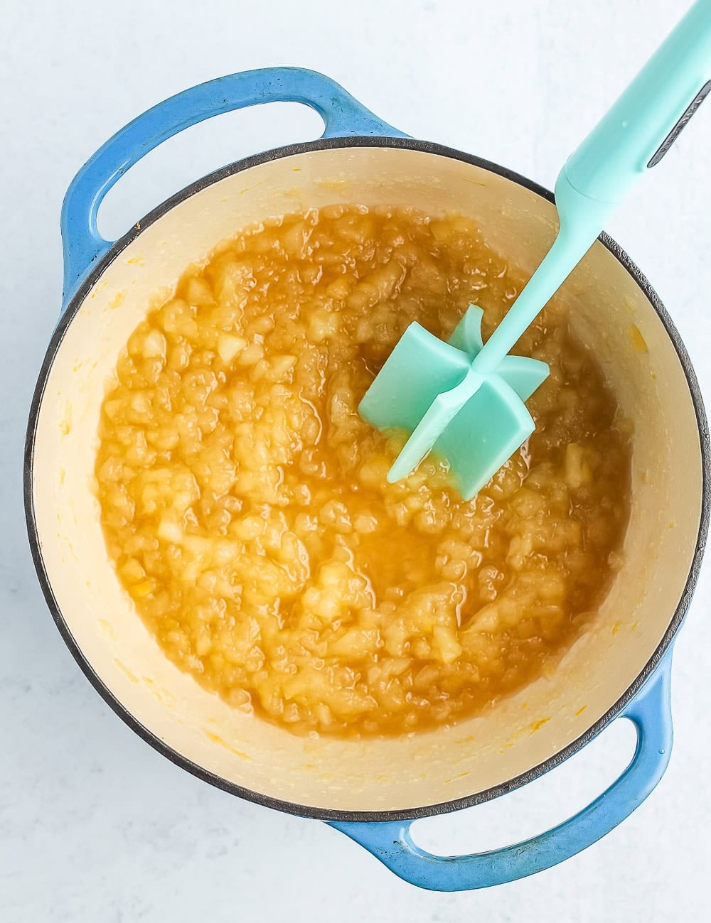 a teal mashing utensil in a blue Dutch oven with chopped fruit.