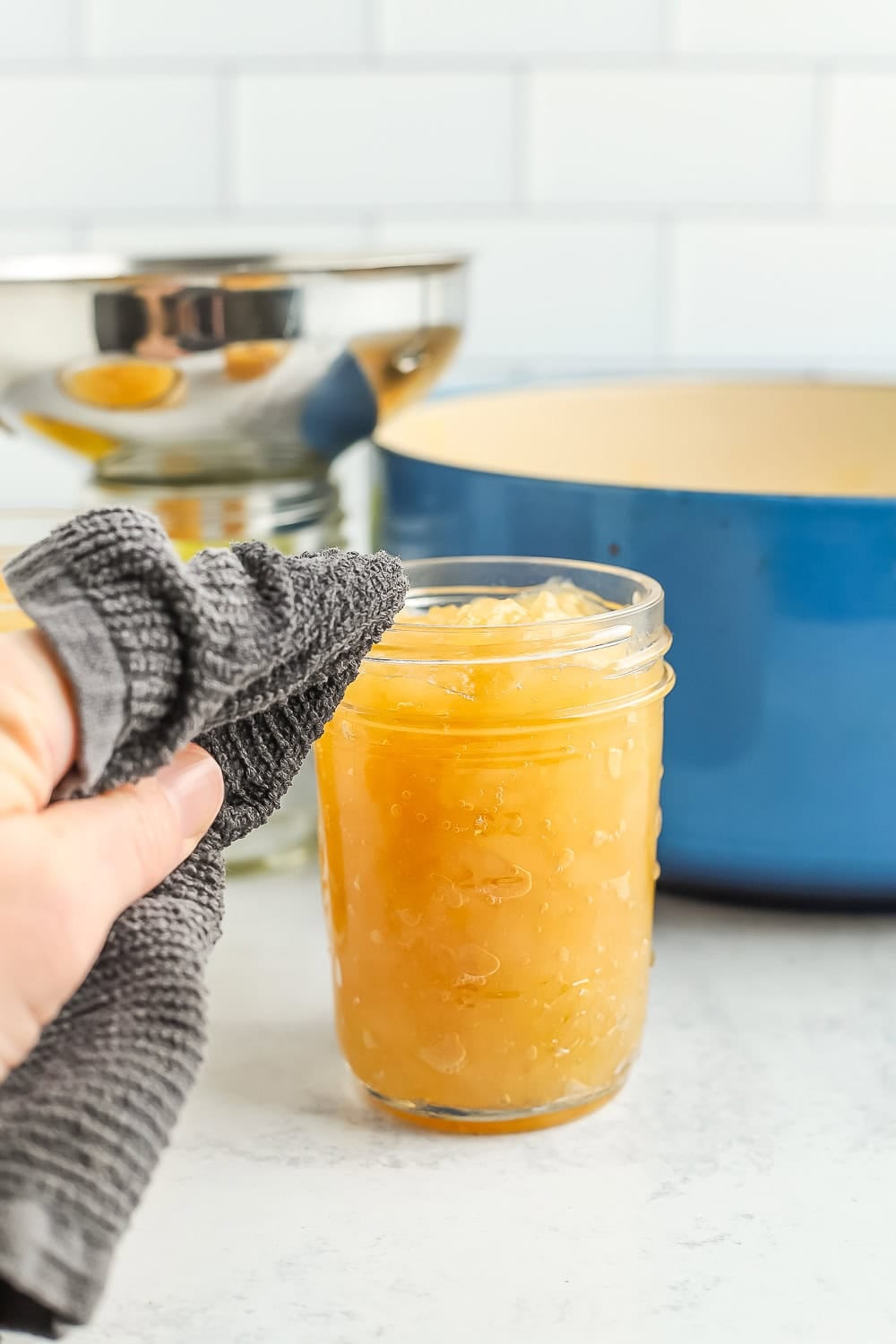a hand with a towel wiping the rim of a canning jar.