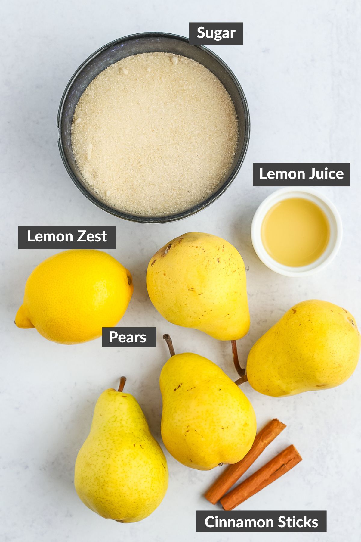 sugar, lemon juice, cinnamon sticks, and pears on a grey board.