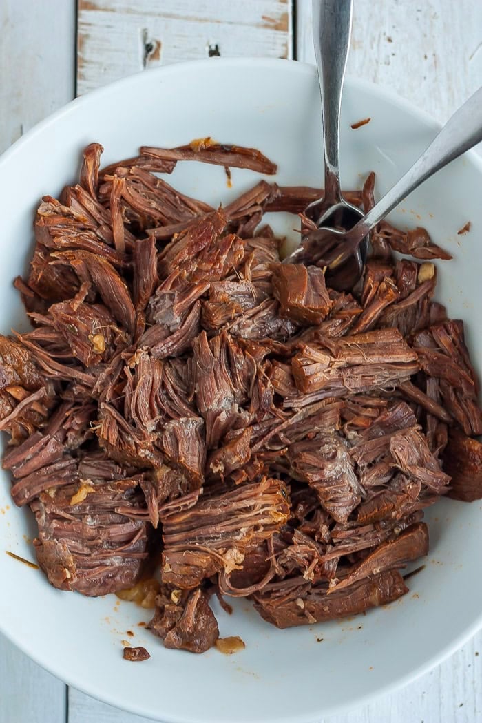 shredded beef in a white bowl with two forks.