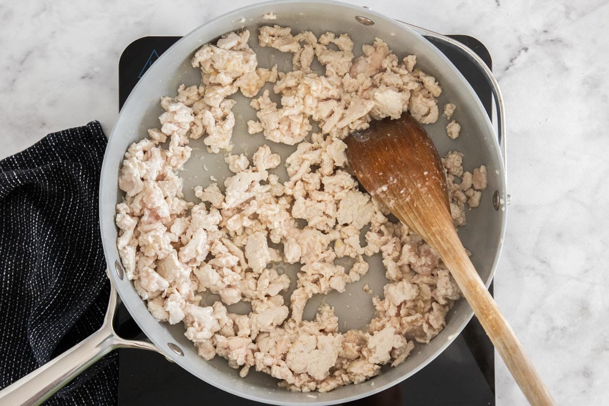 uncooked meat in a skillet with a wooden spoon.