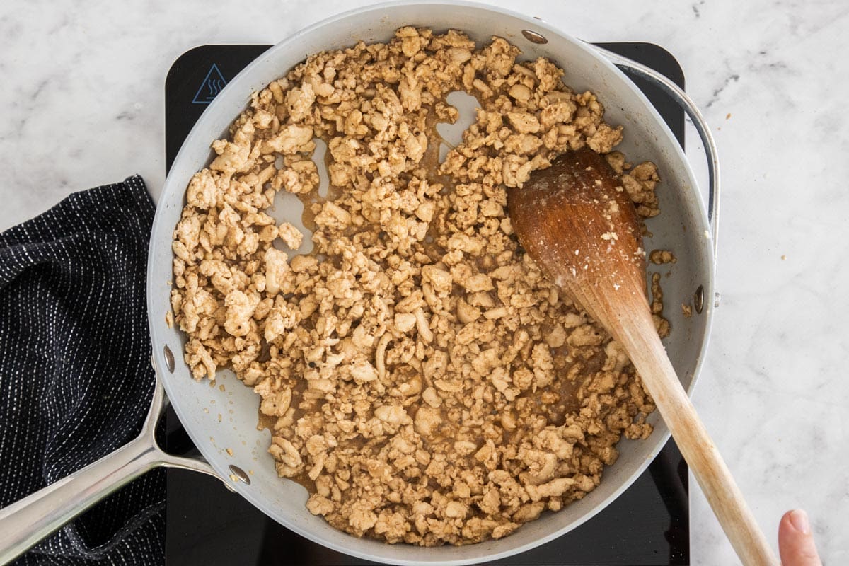 cooked meat and sauce in a skillet with a wooden spoon.