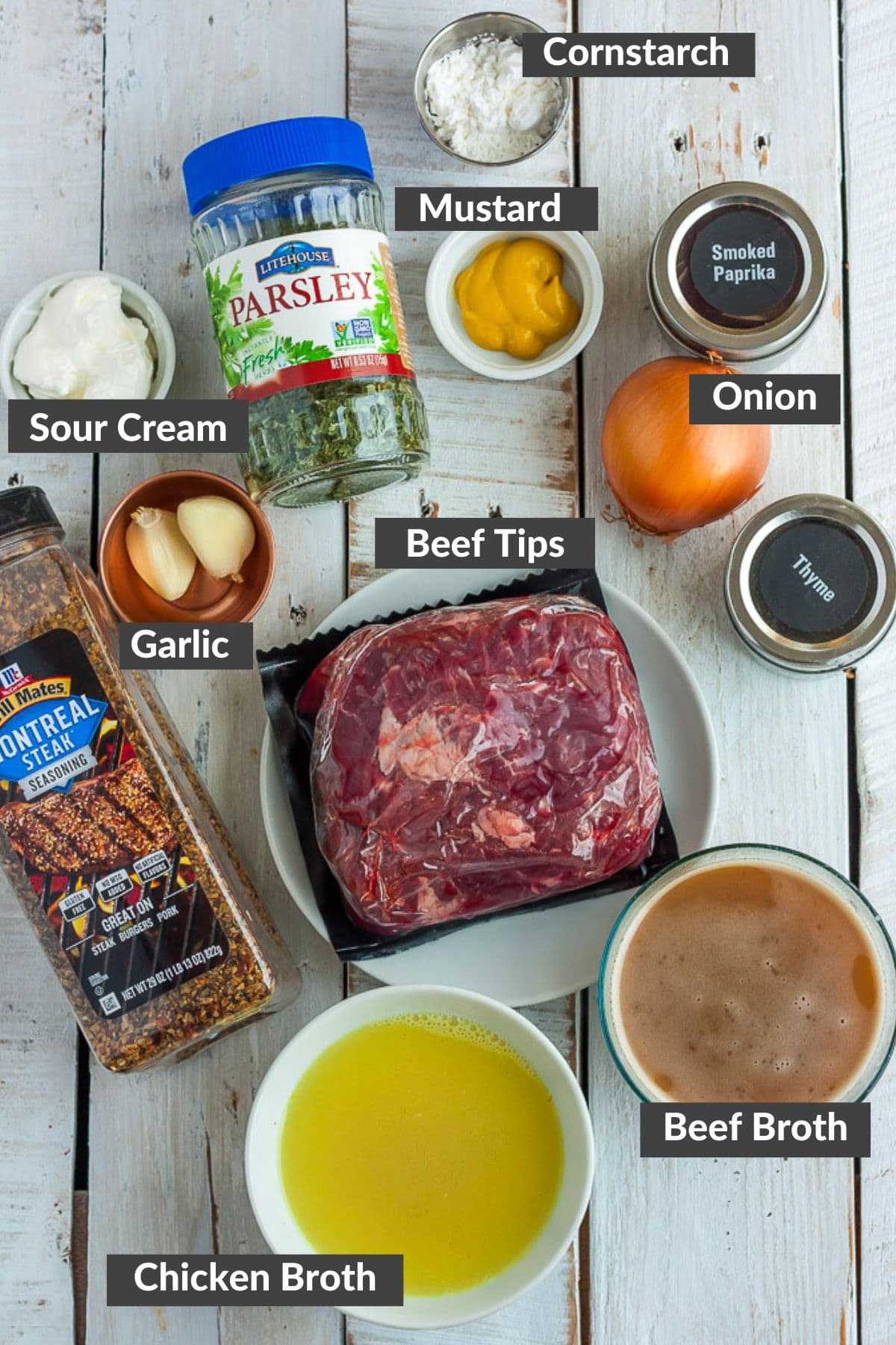 broth, seasonings, garlic, onion, and packaged beef on a white wooden board.