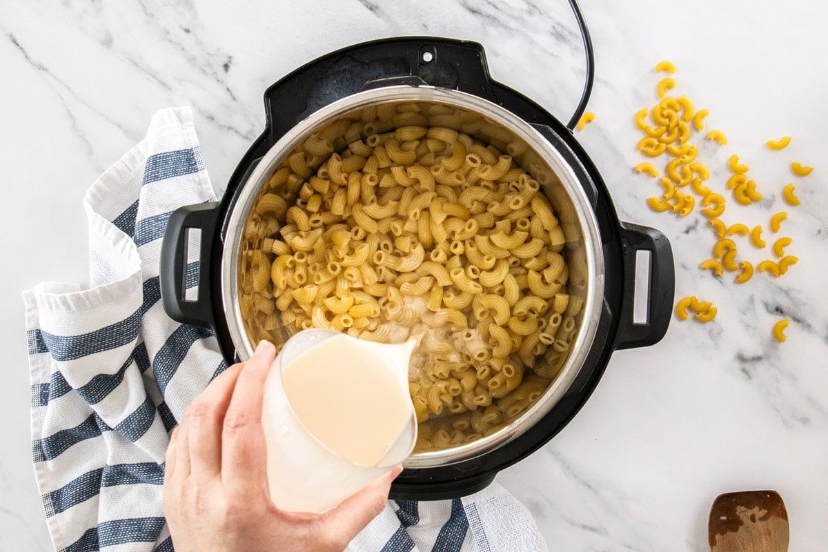 cooked pasta in a pressure cooker with milk being poured in.