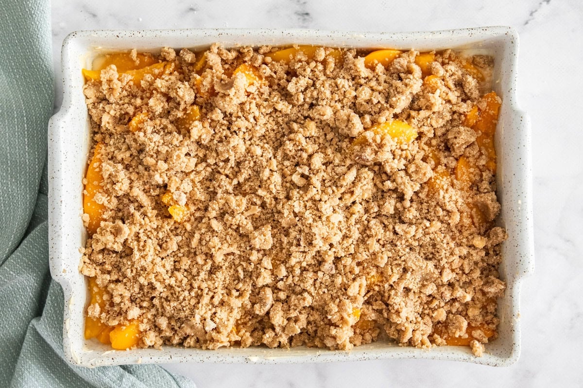 an unbaked peach crisp in a white dish.