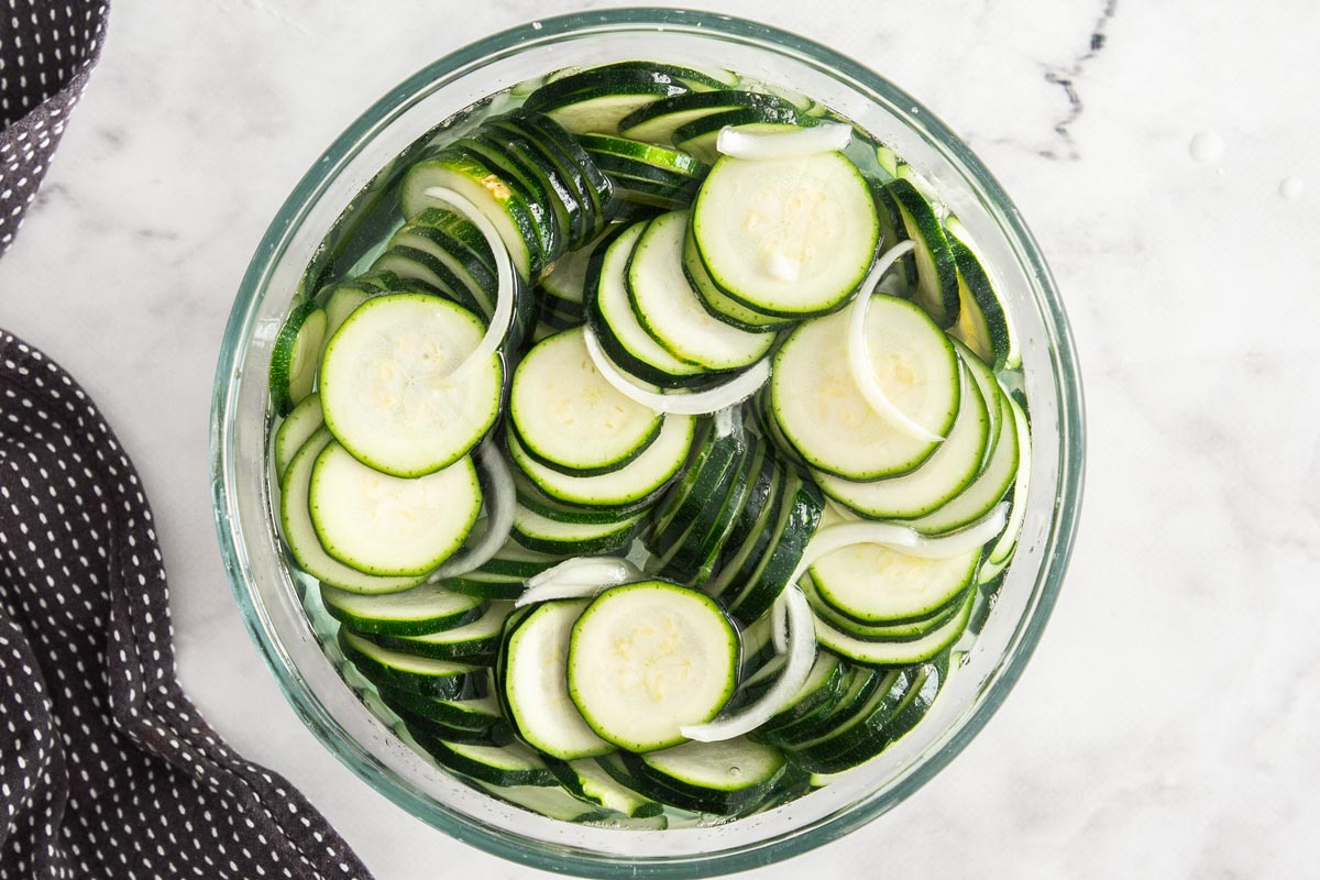 sliced squash and onion in a glass bowl.