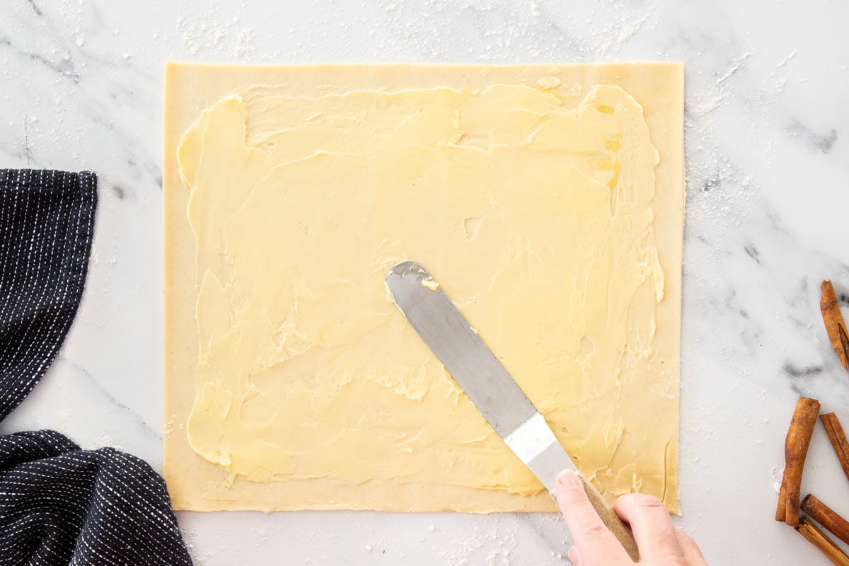 butter being spread on an unbaked piece of dough.
