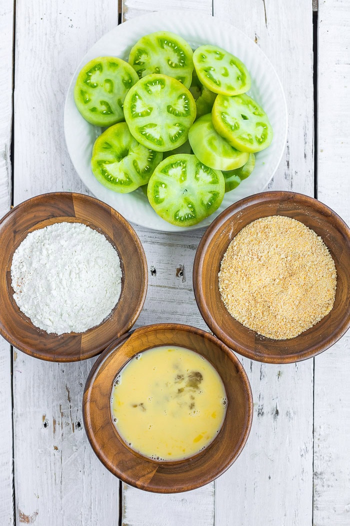 sliced tomatoes and three bowls of ingredients for breading.