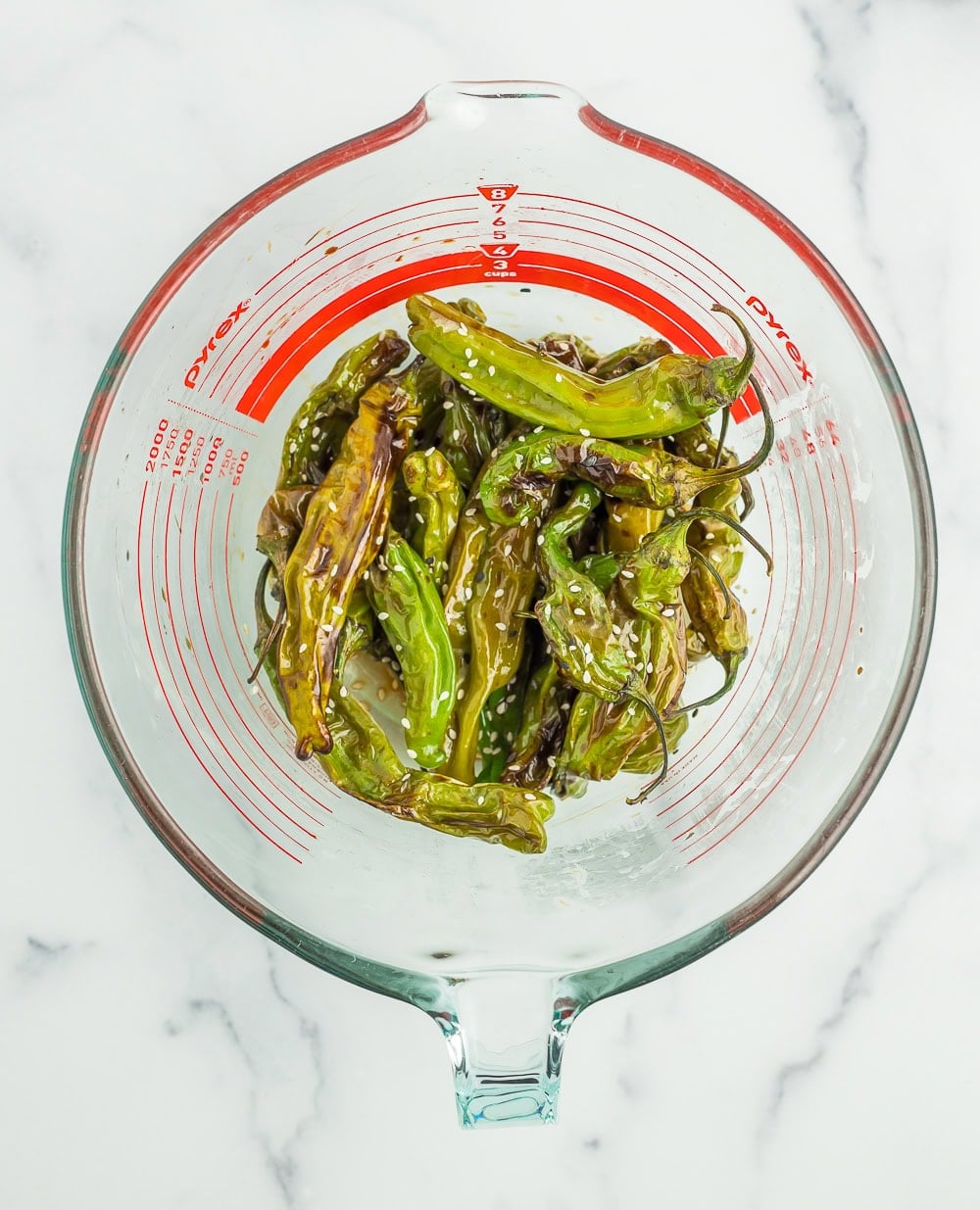 cooked shishito peppers in a glass bowl topped with sesame seeds.