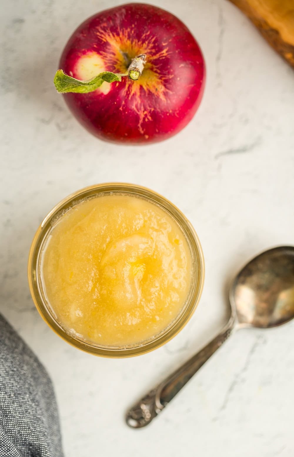 an overhead photo of a jar of apple pie jam with a fresh apple and a spoon.