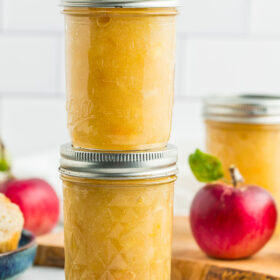 two jars of apple preserves stacked on top of each other with fresh apples.
