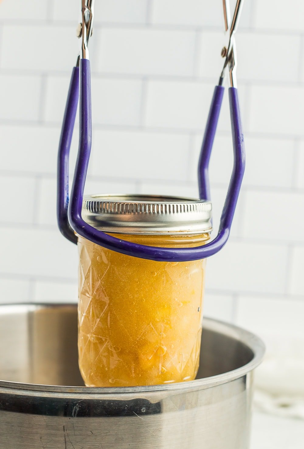 canning tongs lifting a canning jar out of a pot.