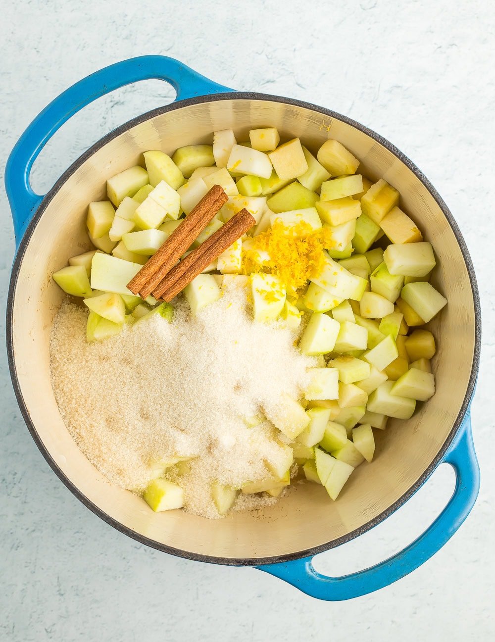 cinnamon sticks, sugar, diced apples, and lemon zest in a blue Dutch oven.