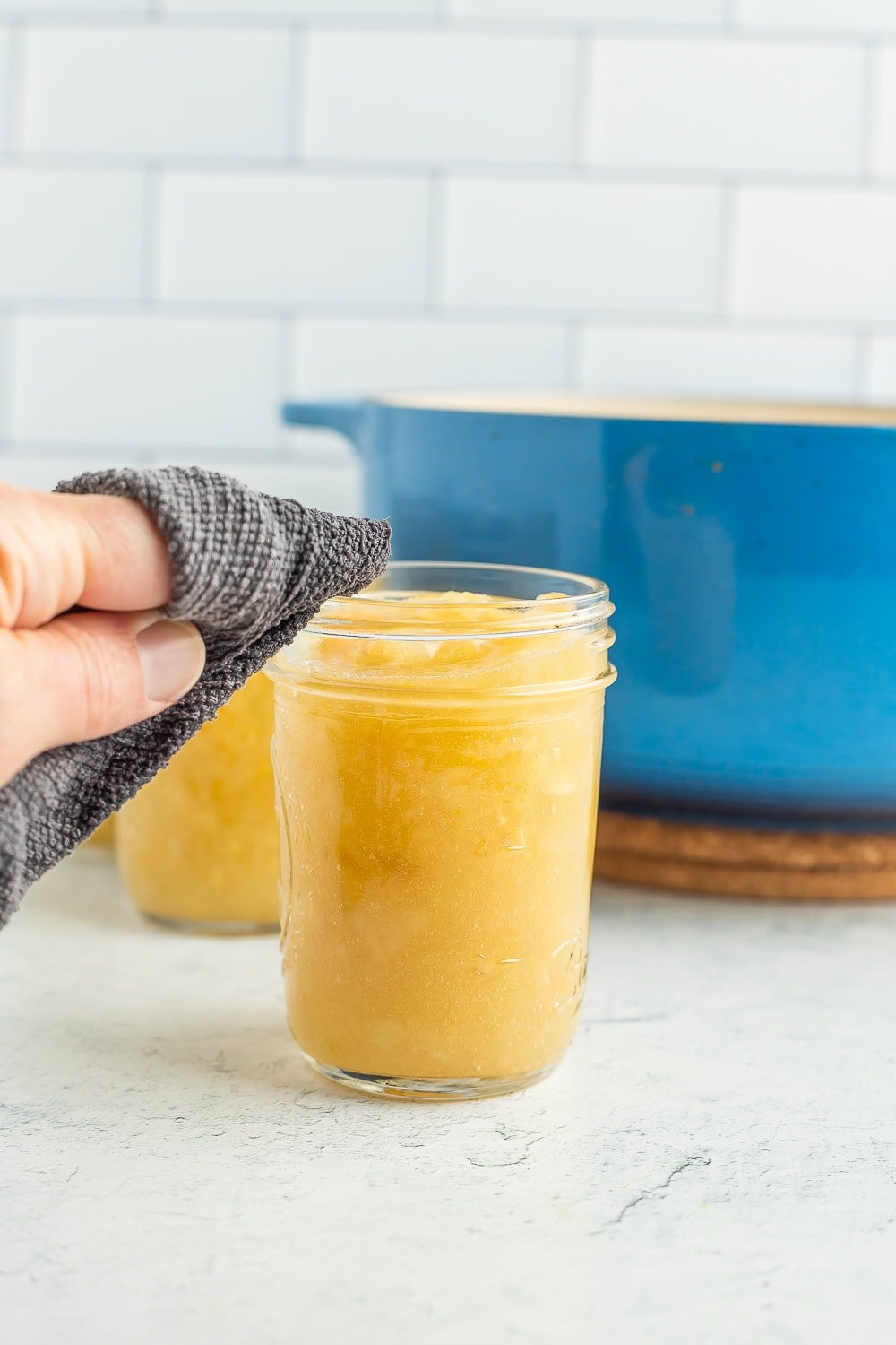 a hand wiping a canning jar with a grey rag.