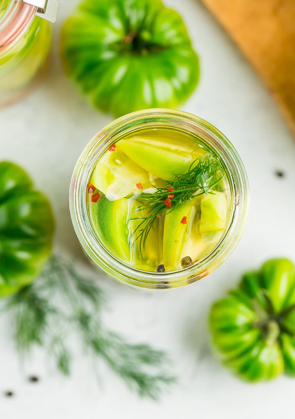 an overhead look into a jar of pickled green tomatoes with fresh dill.
