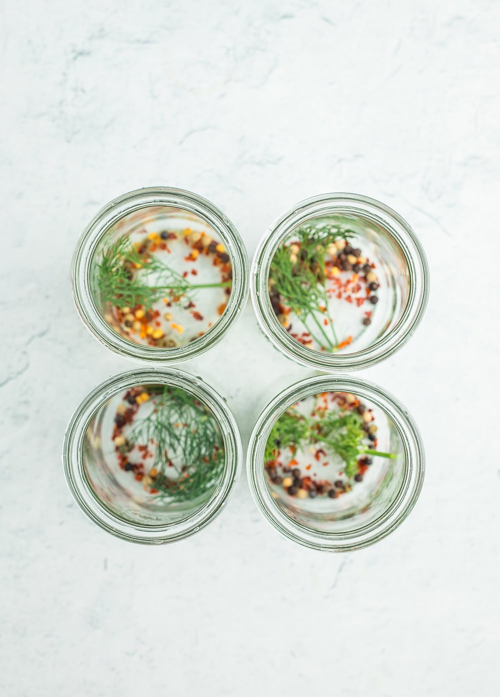 4 glass jars with dill, peppercorns, and red pepper flakes.
