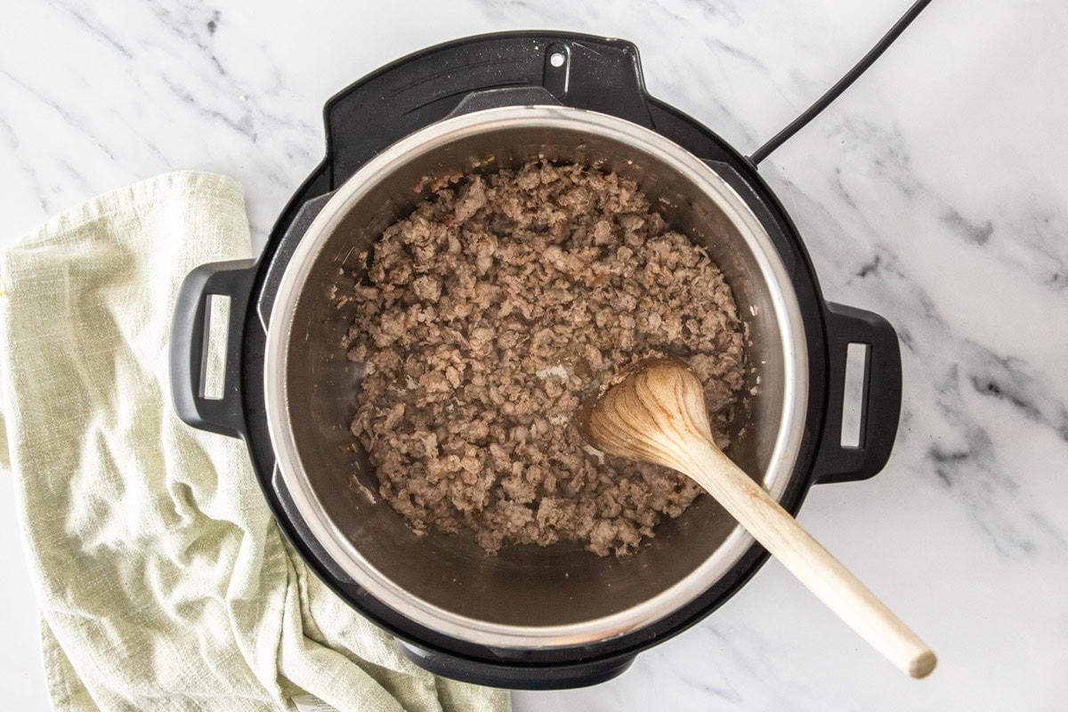 ground sausage in a pressure cooker with a spoon.