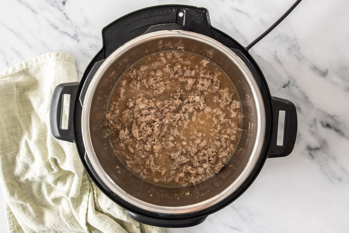 ground sausage and broth in a pressure cooker with a spoon.