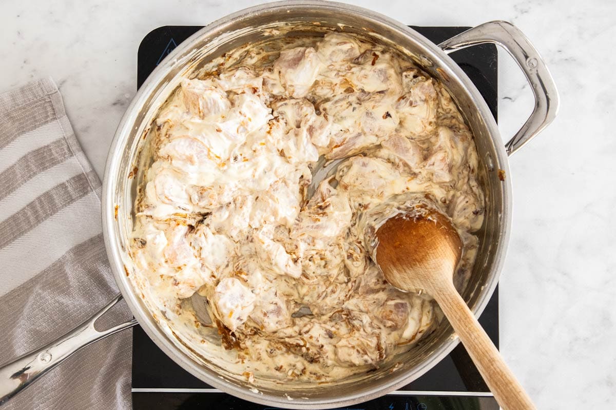 ingredients in a stainless skillet with a wooden spoon.