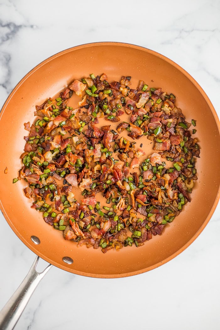 crispy cooked bacon and sauteed peppers in a skillet.