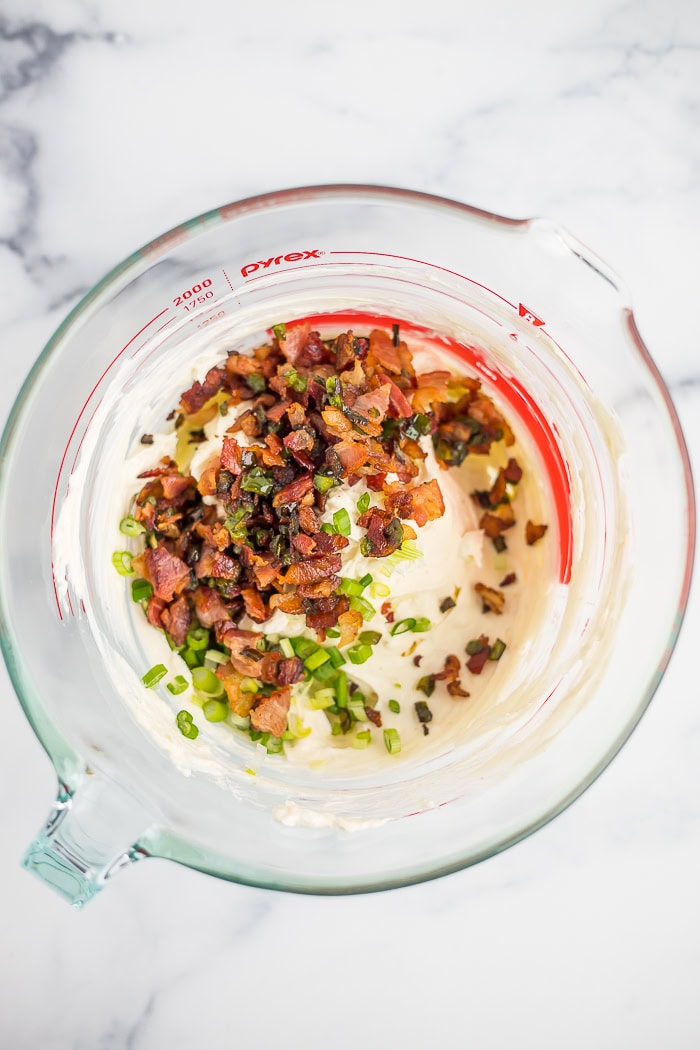 bacon and peppers on top of a cream sauce in a glass bowl.