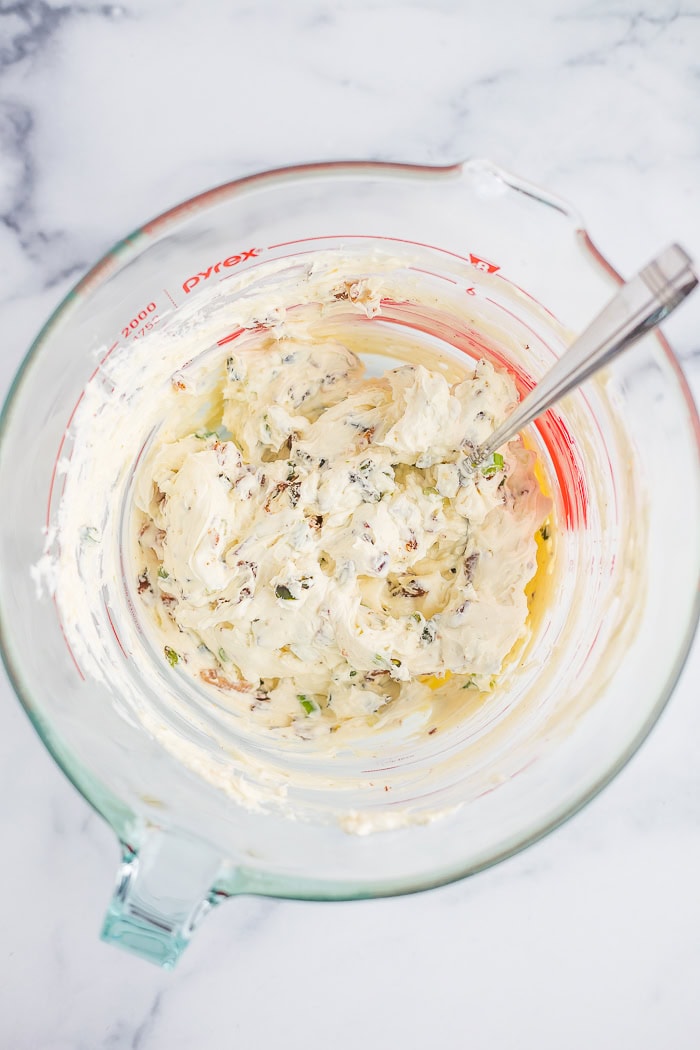 cream cheese, and other ingredients mixed in a glass bowl with a spoon.