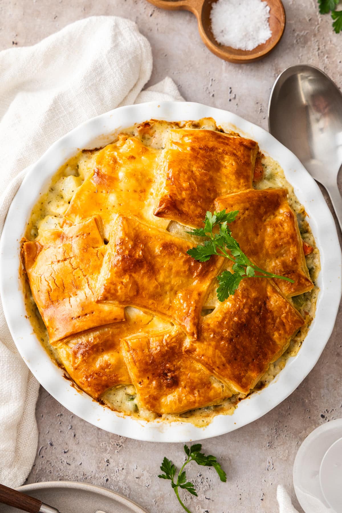 a white pie dish with a baked casserole topped with parsley.