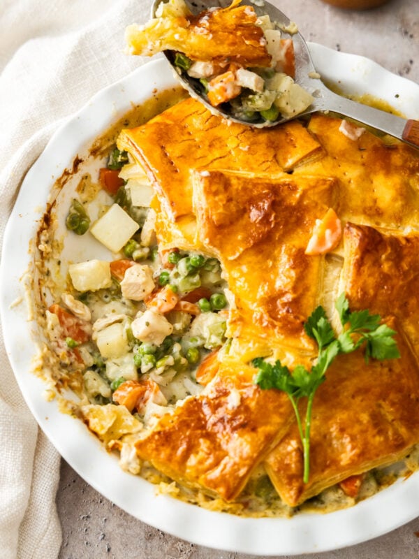 a spoon with a scoop of puff pastry chicken pot pie sitting on a white casserole dish.