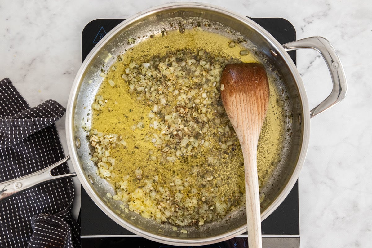 butter, onions, and herbs in a skillet with a wooden spoon.