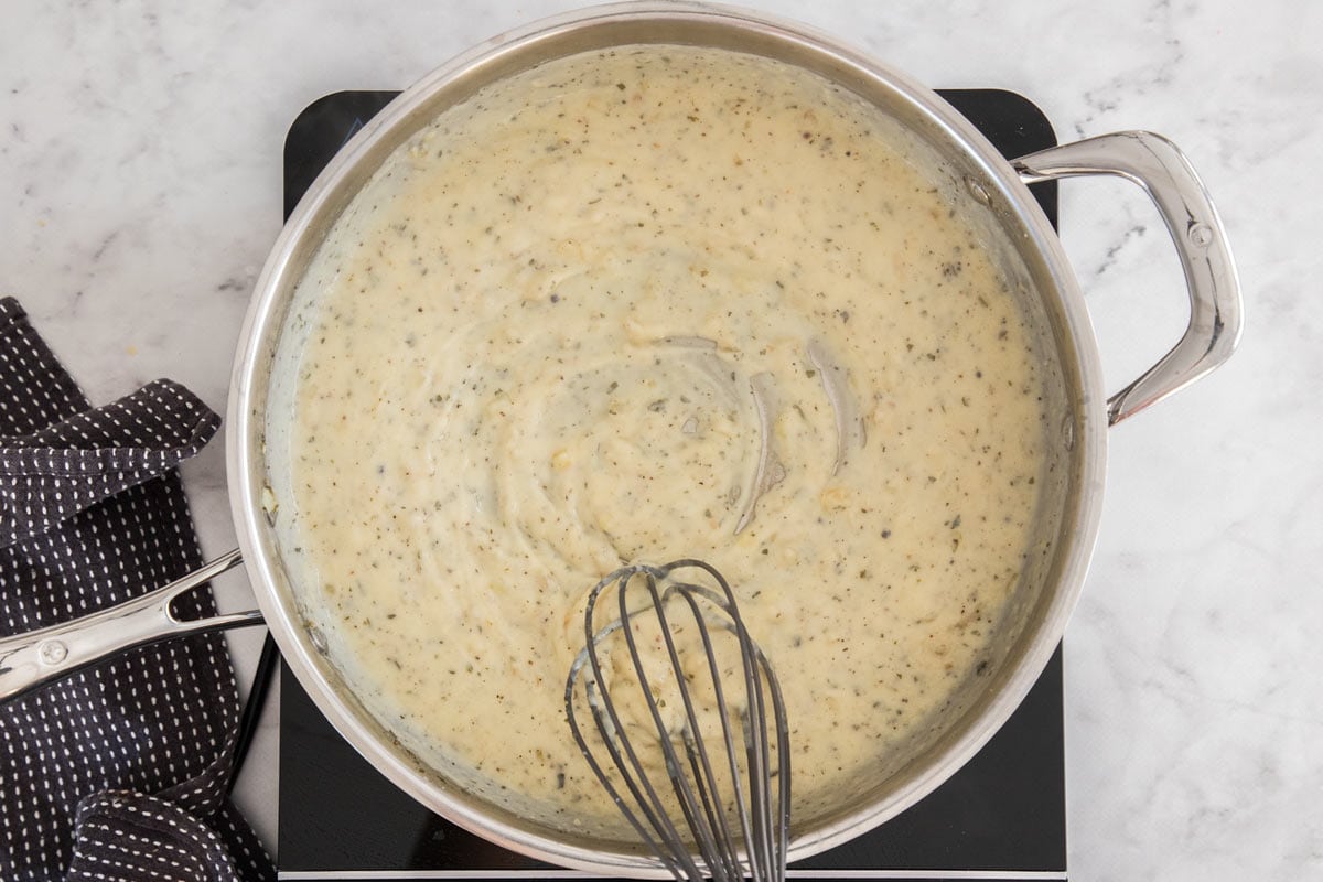 a whisk making a cream sauce in a stainless skillet.