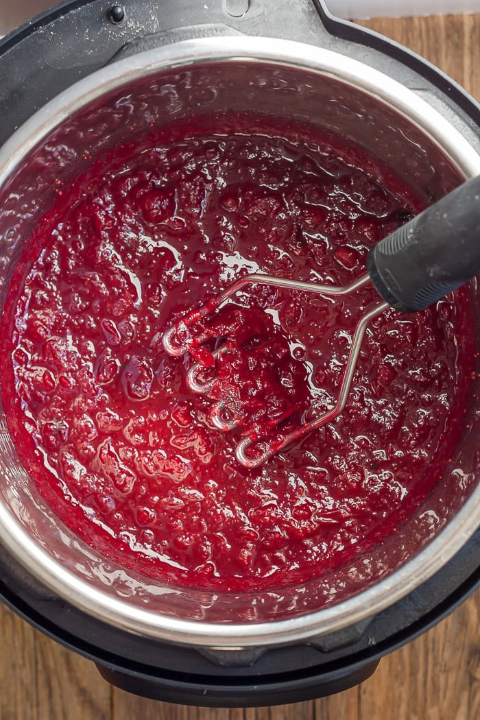 a potato masher making cranberry sauce in a pressure cooker.