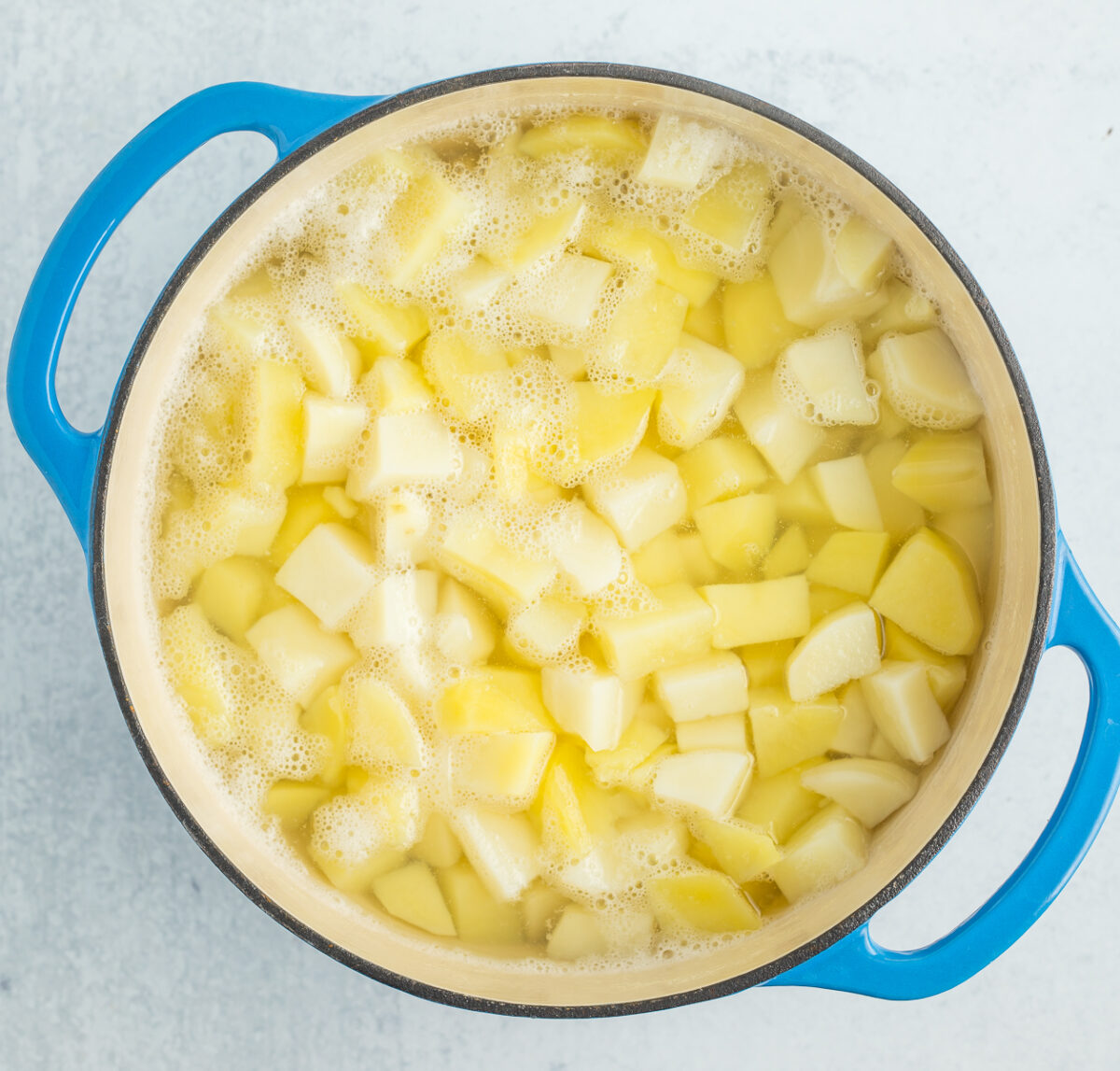 a blue Dutch oven with water and cubed potatoes.